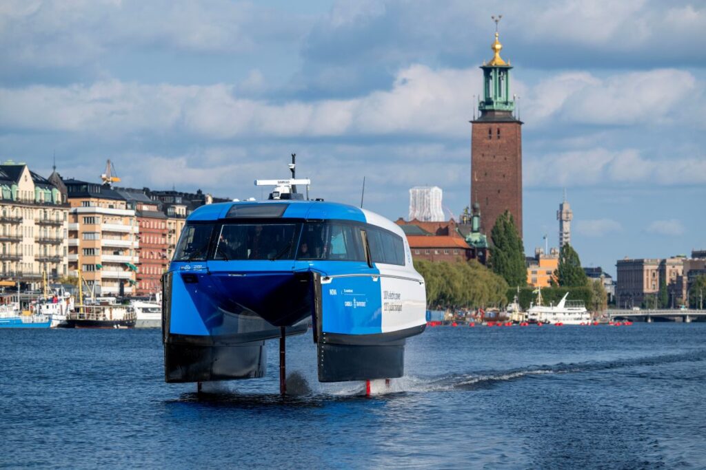 An all-electric Candela P-12 blue and white hydrofoil ferry cruising above the water in Stockholm, Sweden.