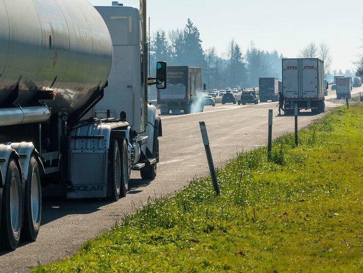 Highway scene shows a tanker and two freight trucks parked on the shoulder of a busy interstate.