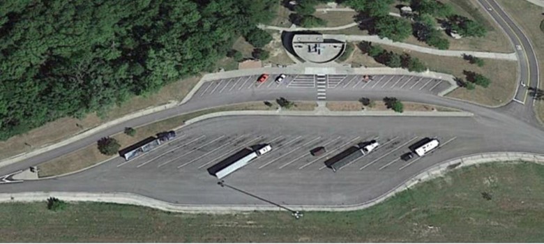Aerial view of a Kansas rest area shows several diagonally parked trucks in long parking slots, with a separate lot containing a few cars in marked parking slots, a main building, and pedestrian walkways