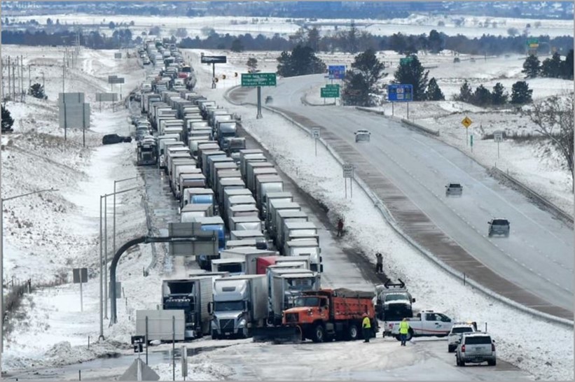 Snowy highway scene shows a massive three-lane traffic jam consisting of tractor-trailers and cars.