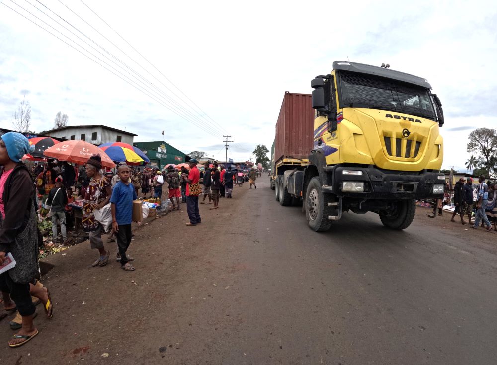 Yellow truck driving down road near public market