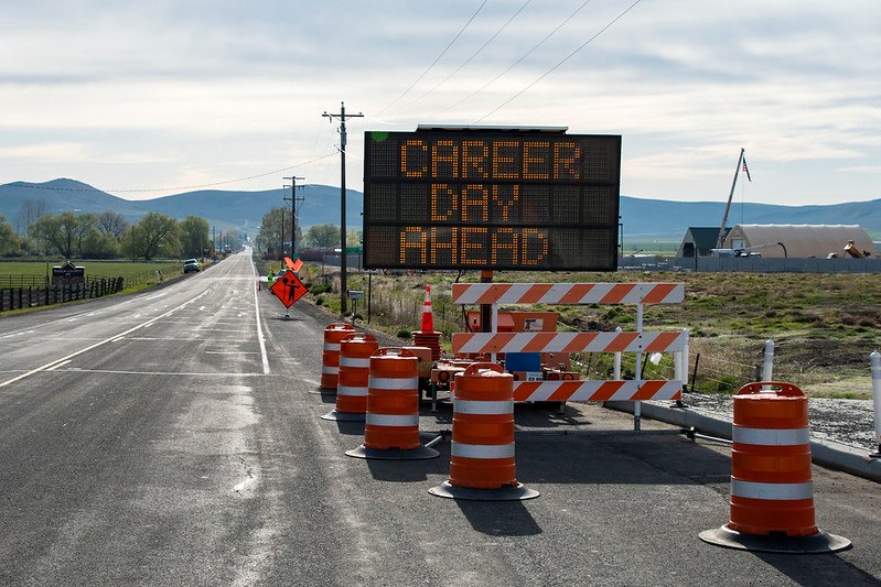 An electronic road sign on a highway reads Career Day Ahead, with traffic barrels and barricades placed nearby.