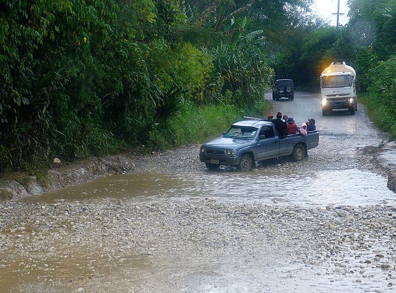 Blue truck approaching deep water-filled pothole on low-volume road