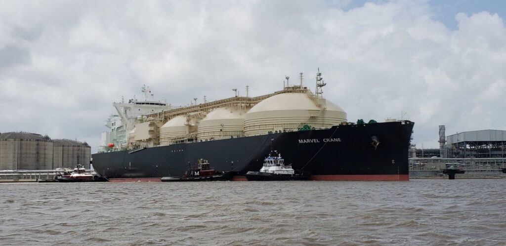 A large liquified natural gas (L N G) carrier named Marvel Crane is guided by tugboats as it moves near a port facility in Louisiana.