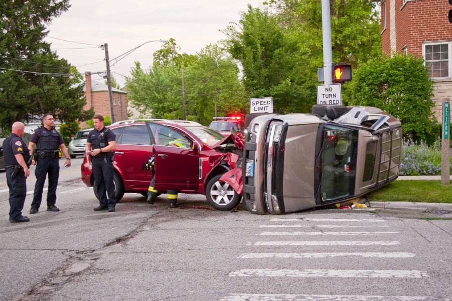 A car lies on its side with crushed roof and side, and another car with a smashed front end is T-boned into it while police officers stand around the intersection crash.