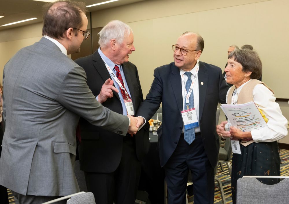 Peter Hendrickson and Paul Skoutelas shake hands while Chris Hendrickson gestures beside them at his son and Katie Turnbull holds papers during the conversation.