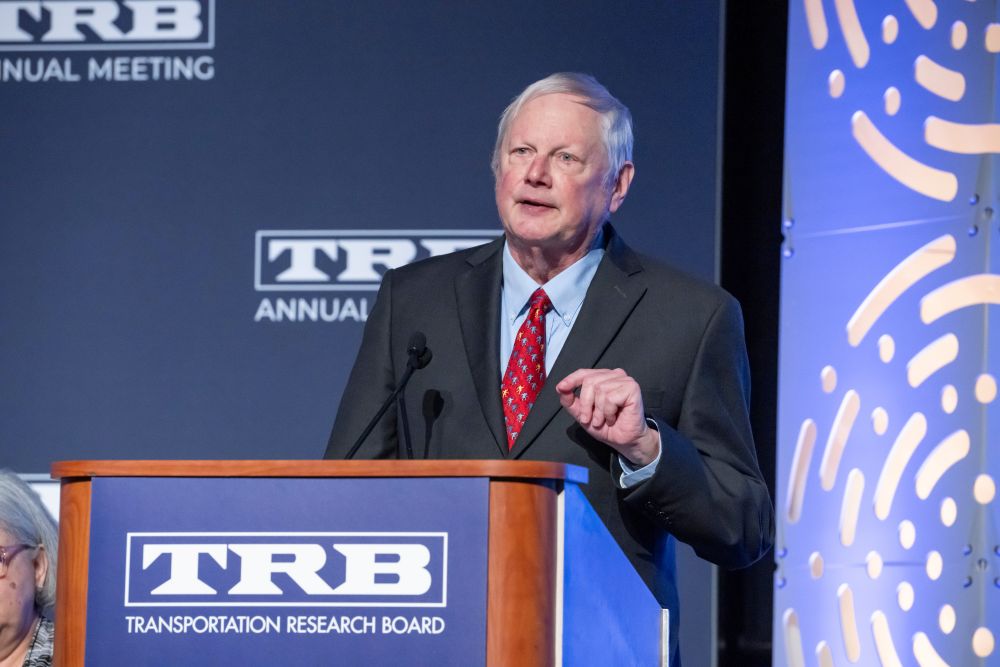 Chris Hendrickson stands at a podium and speaks, with text on the podium reading T R B Transportation Research Board.