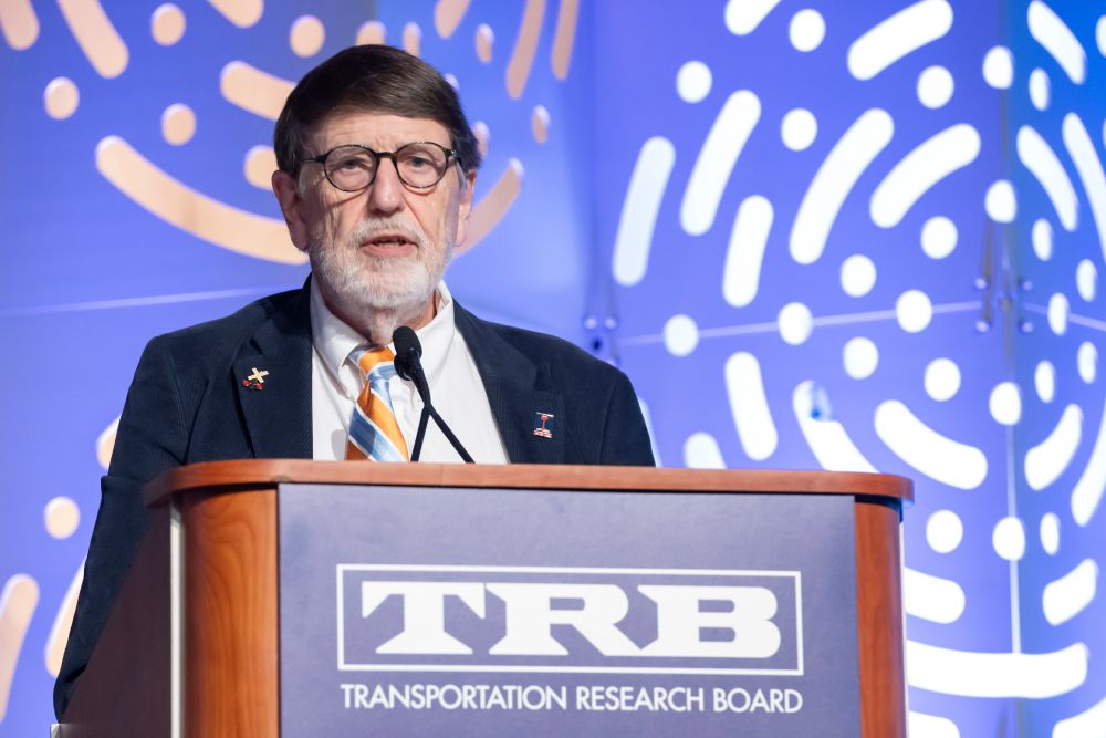 Christopher P. L. Barkan, in formal wear, stands at a podium and speaks, with text on the podium reading T R B Transportation Research Board.