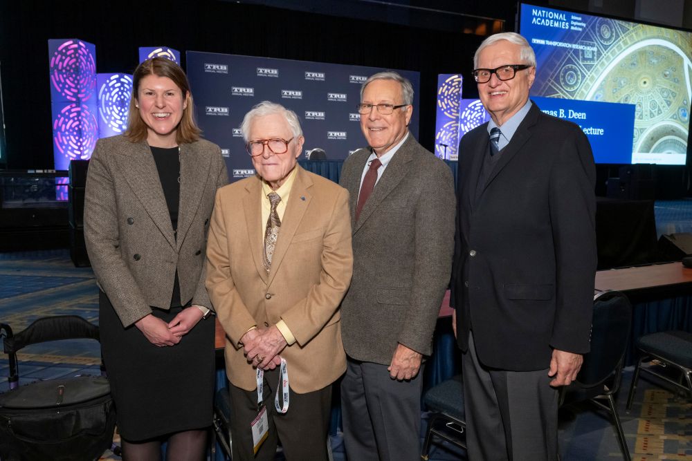 Victoria Sheehan, Thomas B. Deen, Robert E. Skinner, Junior, and Neil Pedersen stand together posing in front of a stage area.
