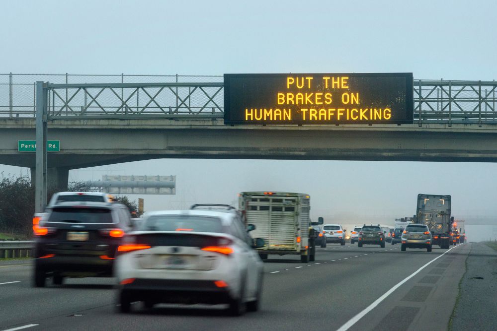 A digital road sign above Interstate 5 in Oregon reads put the brakes on human trafficking. Vehicles drive on the highway below.