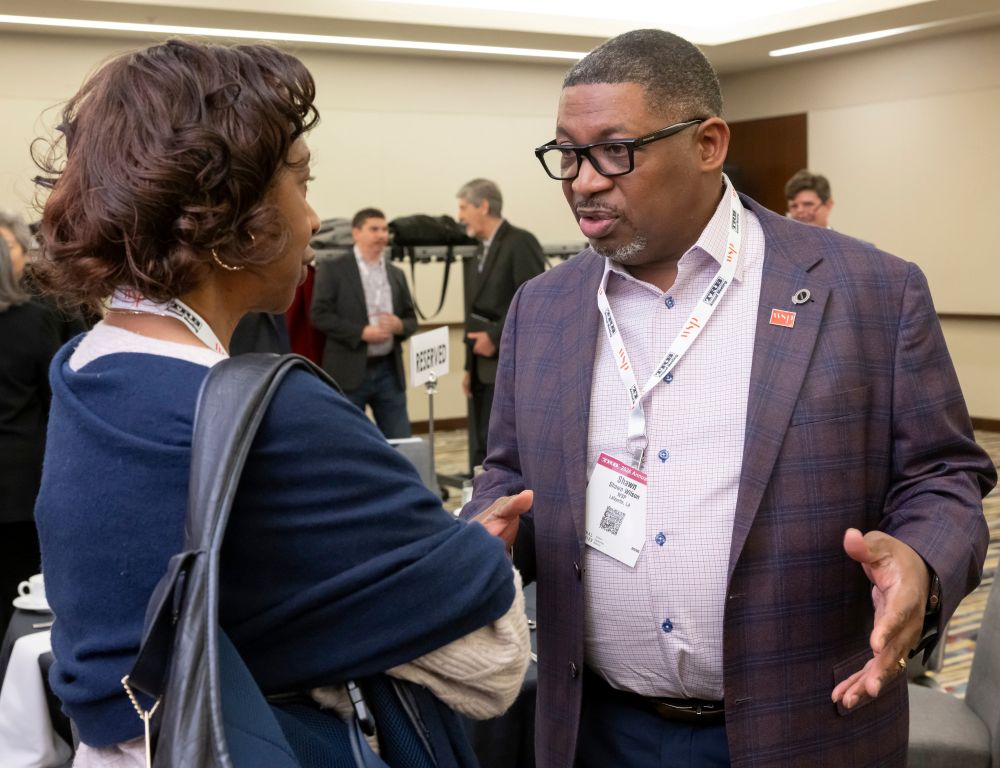Shawn Wilson gestures while speaking with Carol Abel Lewis as they stand facing each other.