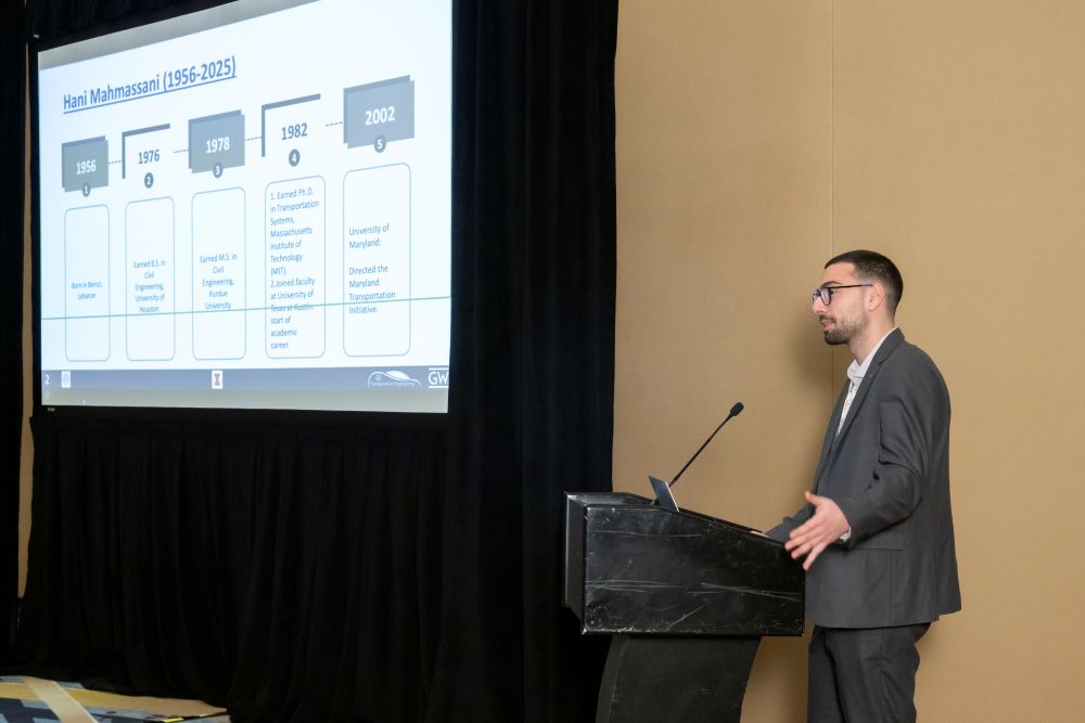Wissam Sleiman, in formal attire, stands at a podium and speaks. A screen shows a timeline with the title Hani Mahmassani, 1956 to 2025.