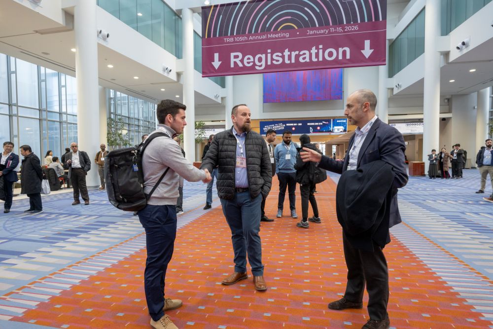 Miguel Muñoz greets Carl Novelli while José Carlos Valdecantos Álvarez gestures during their conversation at the T R B Annual Meeting. A registration banner is in the background.