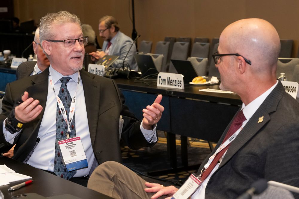 Ricardo Martinez gestures while speaking with Marc Williams as they sit facing each other at a table.