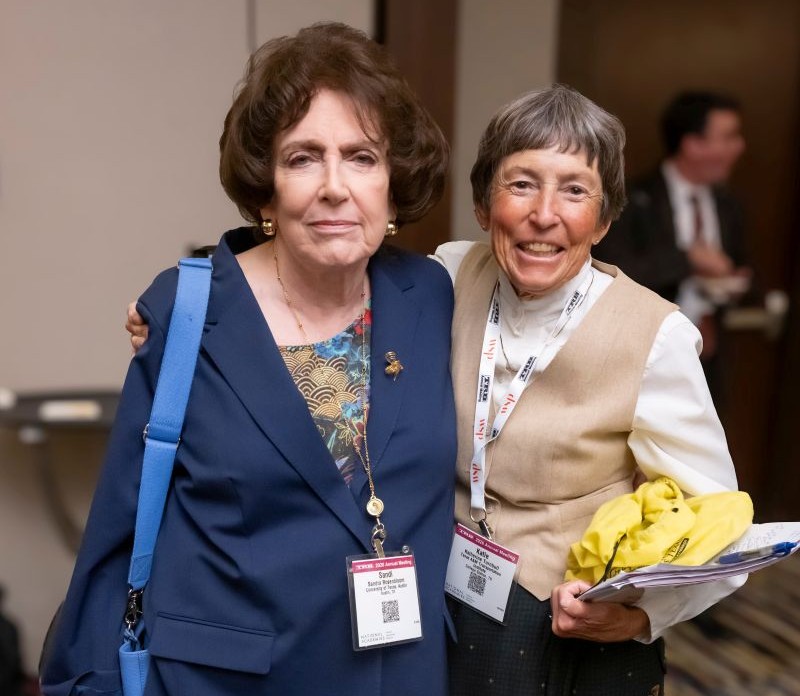 Sandi Rosenbloom and Katie Turnbull stand close together, with Katie Turnbull holding papers and items while both face forward.