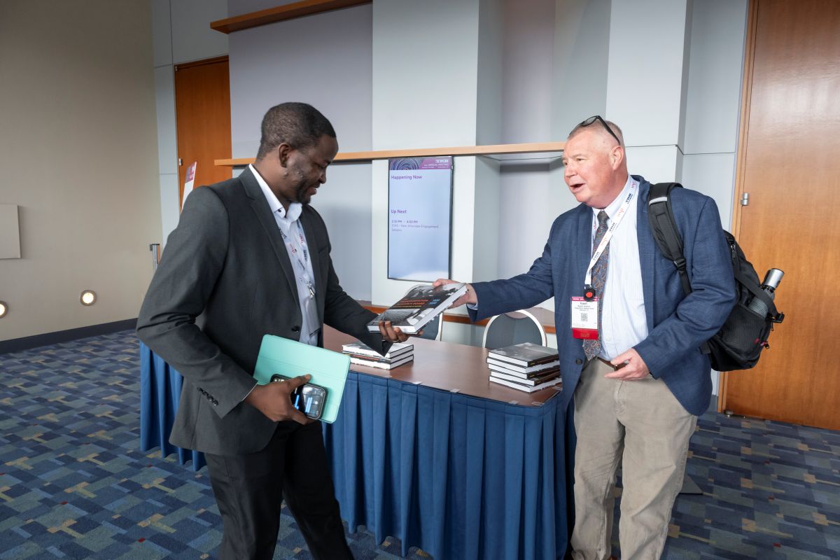 Russell Houston hands a T R B history book to a male attendee.