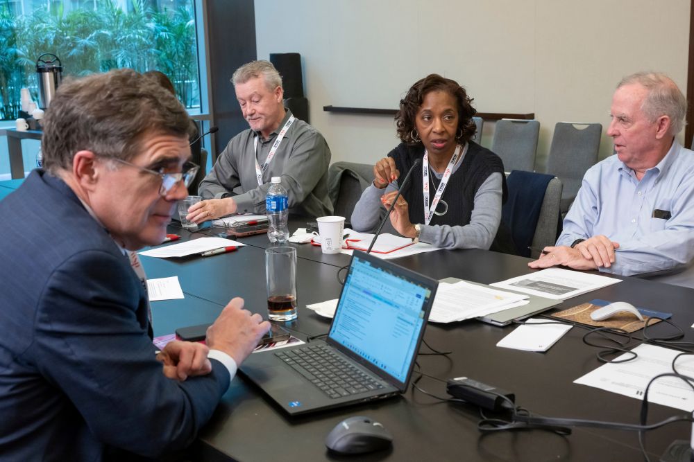 Carol Abel Lewis speaks with Craig Symes, Ricardo Martinez and Craig E. Philip during a T R B Executive Committee meeting. Several documents and a laptop are on the table.
