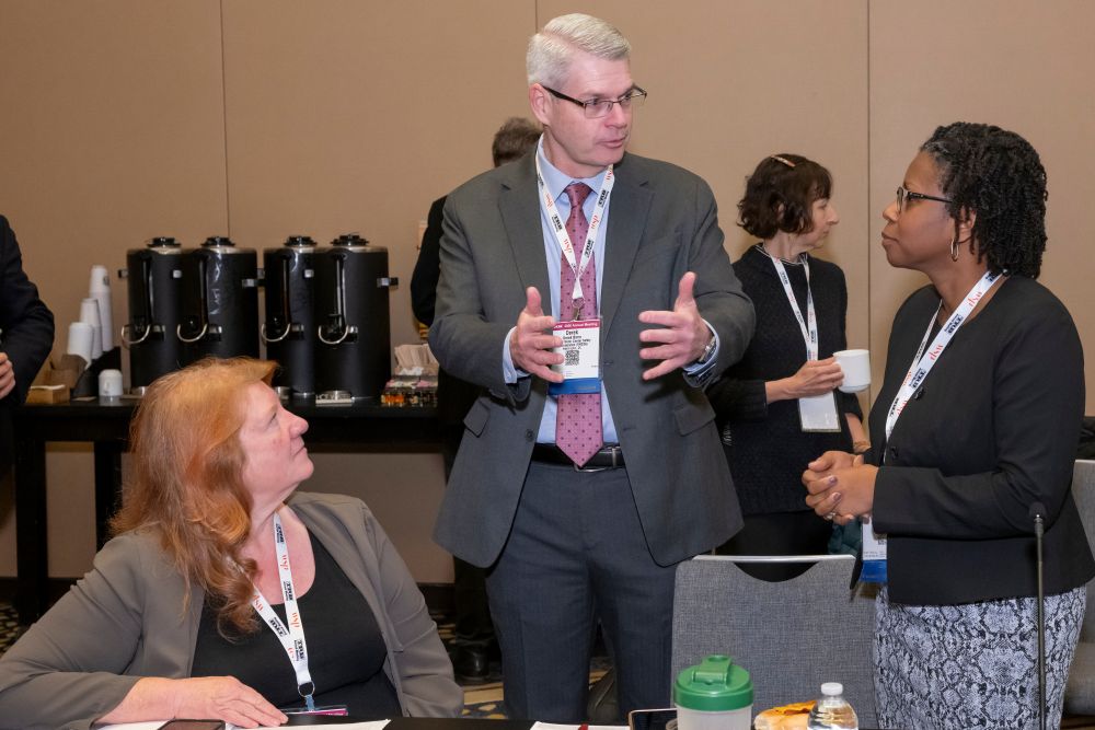 Derek Barrs gestures while speaking with Tracy Larkin Thomason and Shanté Hastings, who stand and sit nearby during a T R B Executive Committee discussion.