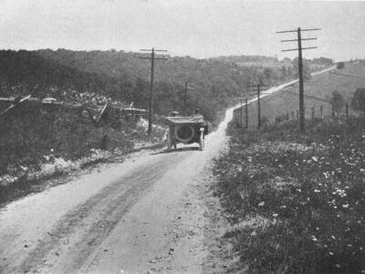 A rural road extends over rolling terrain with utility poles along both sides and a vehicle traveling near the center.