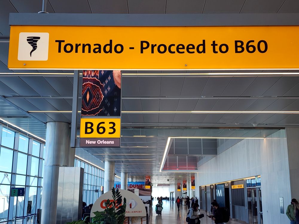 An airport sign directs travelers during a tornado to proceed to B 60, with gate B 63 and New Orleans signage nearby.