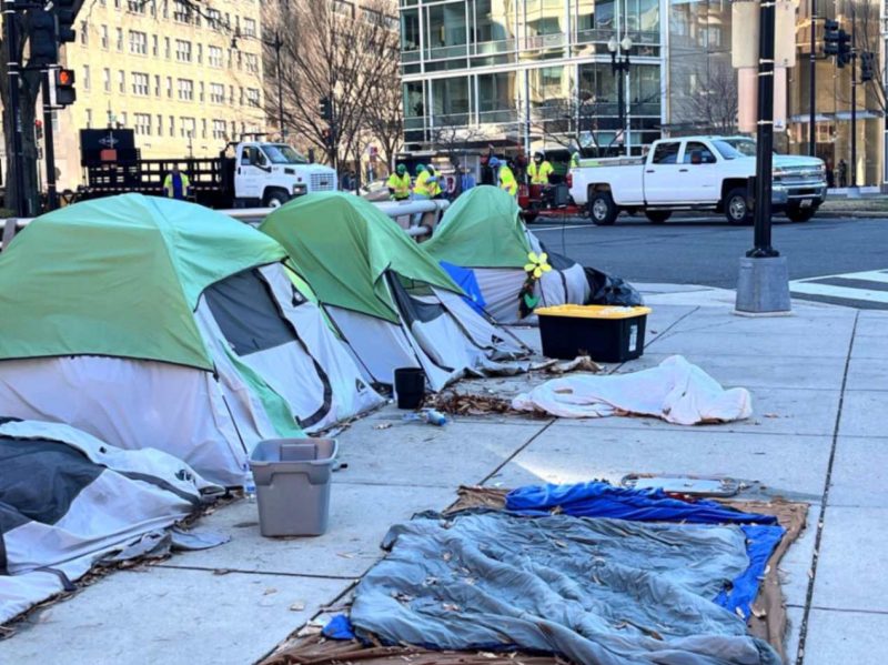22nd Street Homeless Encampment A homeless encampment of four tents, a wet sleeping bag, and plastic container boxes occupy a sidewalk in Washington, DC.