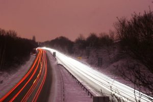 Headlights and taillights form ribbon-like streaks along a divided highway in a time-lapse photo taken at sunset.