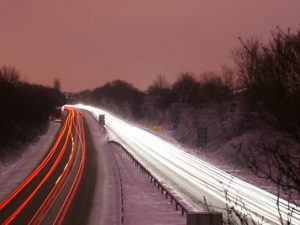 Headlights and taillights form ribbon-like streaks along a divided highway in a time-lapse photo taken at sunset.