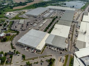 An aerial view of a large distribution center shows freight trucks at docks and in large parking lots within a residential community,