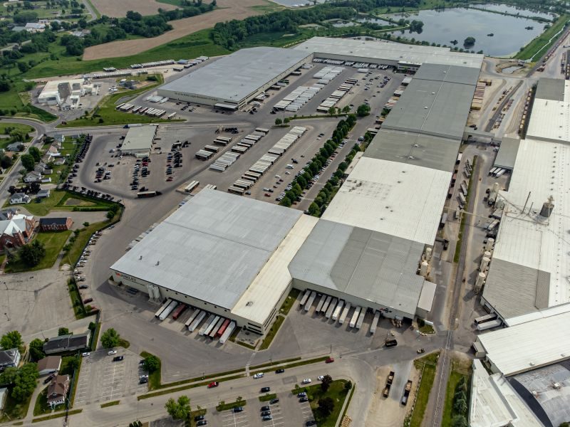An aerial view of a large distribution center shows freight trucks at docks and in large parking lots within a residential community,