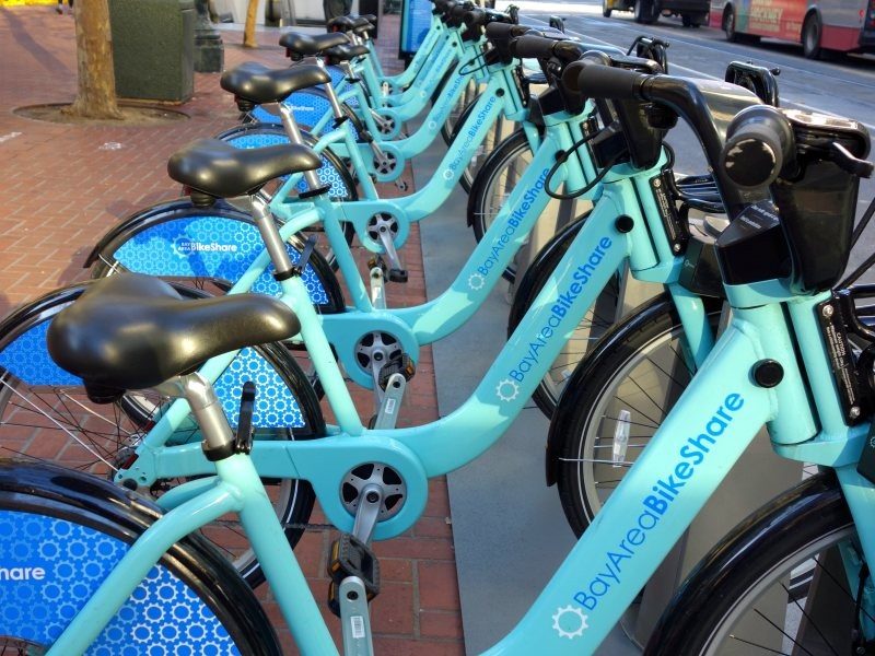 Flatworld Bay Area BikeShare A close view of a fleet of bicycles parked at a bike-sharing location in San Francisco, California. The text on the bicycles reads 'Bay Area Bike Share.'