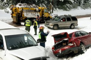 Police and emergency workers respond to a snowy road crash in Oregon involving multiple vehicles, while a snowplow truck clears the road in the background.