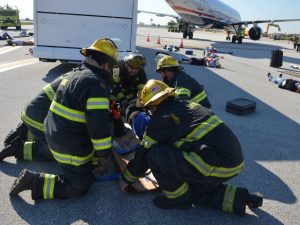 Firefighters provide emergency care to a person on the airport apron near a passenger airplane during an emergency response exercise.