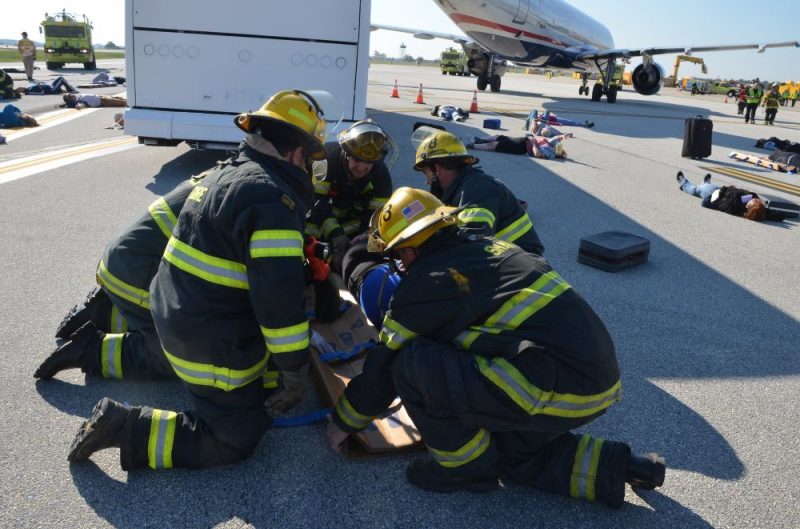 Firefighters provide emergency care to a person on the airport apron near a passenger airplane during an emergency response exercise.