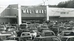 A crowded parking lot filled with 1980s cars stands in front of a Wal-Mart store with Discount City signage.