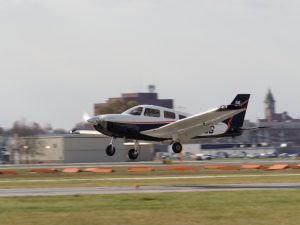 A small propeller aircraft flies just above a runway with its landing gear extended.